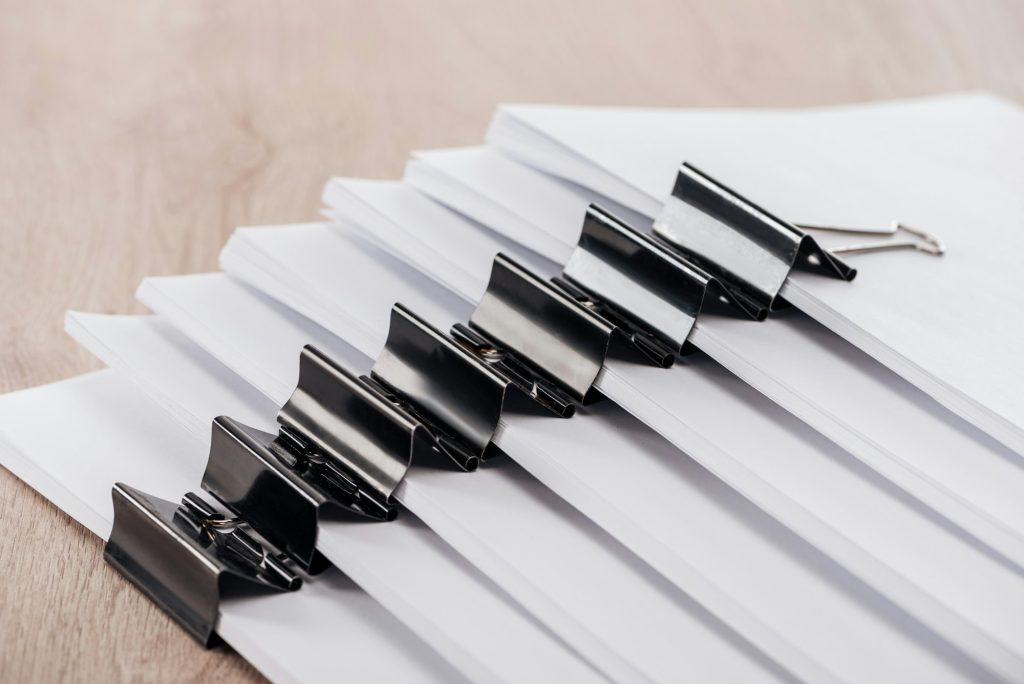 arranged stacks of blank paper with metal binder clips on table